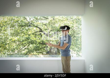 Man using VR headset at window with view of tree Stock Photo