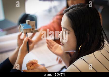 Female architect discussing house model with colleagues in meeting Stock Photo