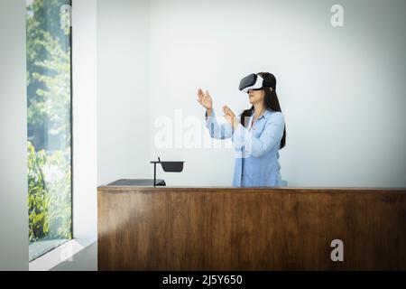 Businesswoman using VR headset behind desk in office Stock Photo