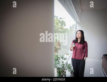 Thoughtful young woman drinking tea in window at home Stock Photo