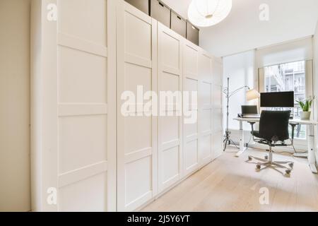 Laptop and computer placed on table near window in light stylish home office with closed white closet in modern apartment Stock Photo