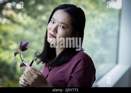 Portrait smiling young woman holding branch at window Stock Photo