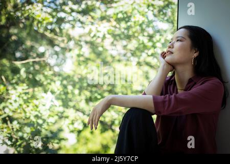 Thoughtful young woman looking at tree from window Stock Photo