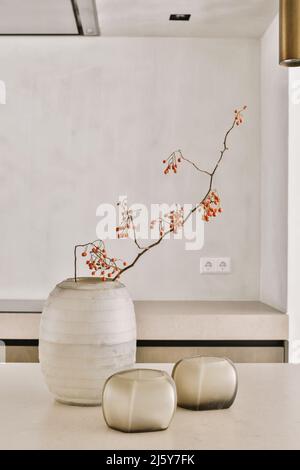 Thin twigs with orange berries in elegant vase placed on table near candles in modern minimalist style room Stock Photo