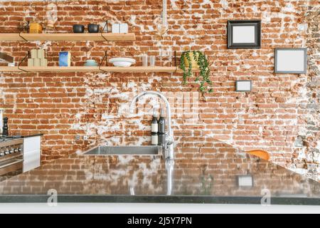 Side view of a black mirrored countertop and sink and in the background a brick wall with shelves and pictures Stock Photo