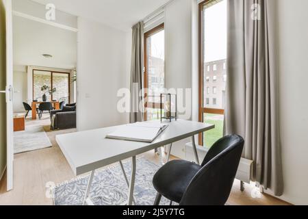 White table with opened book placed on rug near windows in light spacious home office with decorative frames in flat Stock Photo