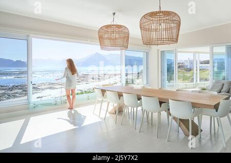 Woman enjoying ocean view from sunny modern dining room Stock Photo
