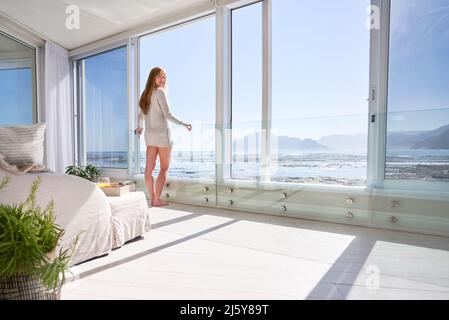 Portrait young woman standing at open patio door with sunny ocean view Stock Photo