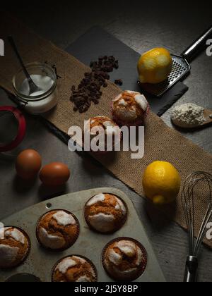 Top view of tasty freshly baked muffins served on table with lemons and sugar near chocolate drops in light kitchen Stock Photo