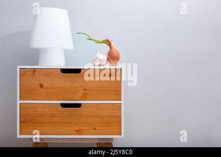 Stylish side table with wooden drawers and lamp and two onions on top placed on gray background in light room Stock Photo