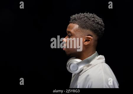 Young African American man in glasses with headphones on neck and looking at camera against black background Stock Photo