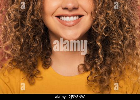 Crop unrecognizable Woman portrait with curly hair smiling and looking at camera while standing on pink background Stock Photo