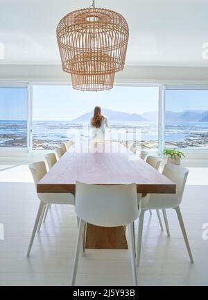 Woman standing at open dining room patio door with ocean view Stock Photo