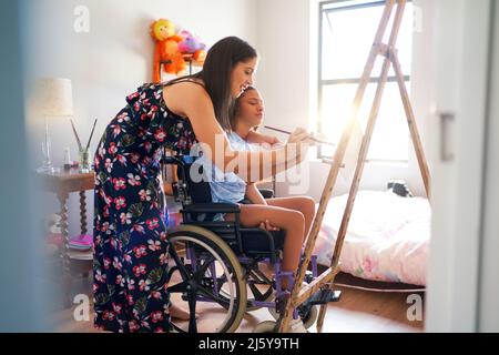 Mother and disabled daughter in wheelchair painting in bedroom Stock Photo