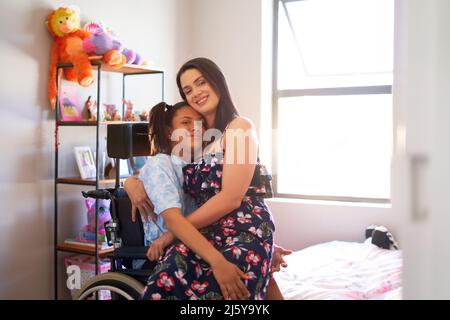Portrait happy, affectionate mother hugging disabled daughter at home Stock Photo