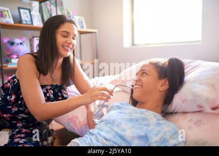 Mother helping disabled daughter drinking water from straw on bed Stock Photo