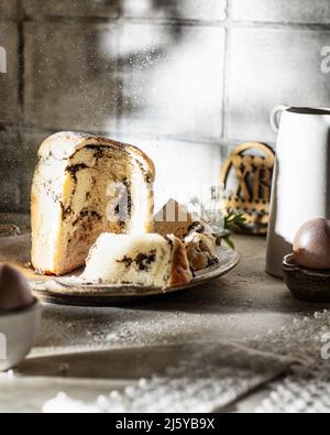 Easter cake with poppy seed filling sliced on festive table with powdered sugar. Still life with Easter table, Easter cake and painted eggs. National Stock Photo