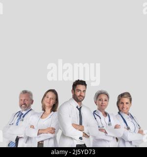 Group of successful medical doctors in labcoat uniform standing together with arms folded isolated on gray background with copy space for text Stock Photo
