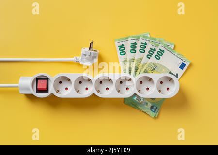 White power strip on 100 euro banknotes and white electric plug over yellow background. Rising energy costs due to power crisis. Inflation concept. Stock Photo