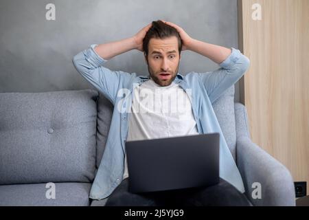 Perplexed and confused bearded businessman staring at the laptop screen and makes a helpless gesture. Hipster man in casual clothes looking at monitor with asking expression Stock Photo