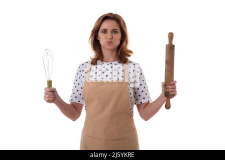 Horizontal shot of confident cheerful beautiful young woman in apron holding rolling pin and whisk in both hands, isolated on white background. Stock Photo