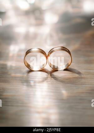 Golden wedding rings with shining bokeh on wooden surface, eternal love concept. Closeup Stock Photo