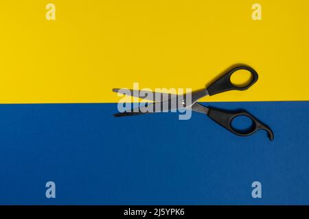 a pair of scissors on a blue and yellow bicolor background Stock Photo