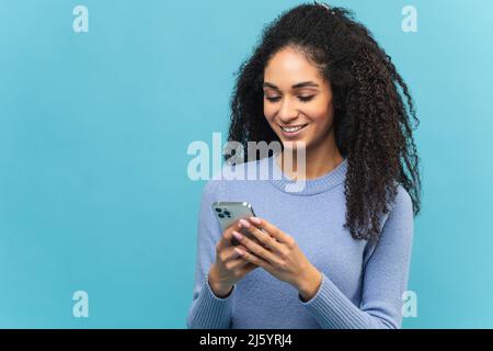 Attractive young multiracial woman webbrowsing on smartphone, millennial female chatting on social networks, using mobile app, texting online with friends, sharing news, isolated on blue Stock Photo