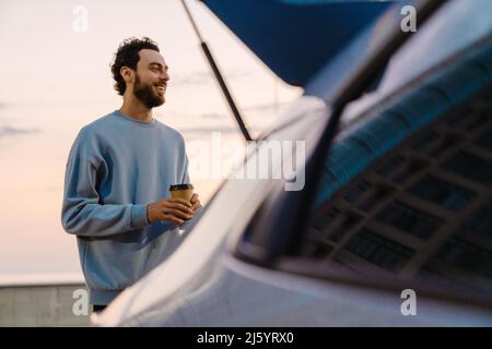 Young man smiling while drinking coffee on parking outdoors Stock Photo