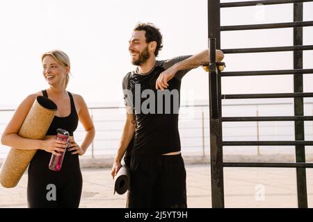 Young man and woman smiling while working out together on sports ground outdoors Stock Photo