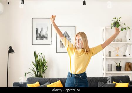 Charming elegant mature middle-aged businesswoman smiling, sitting in the modern house, wearing yellow sweater. Happy people concept Stock Photo