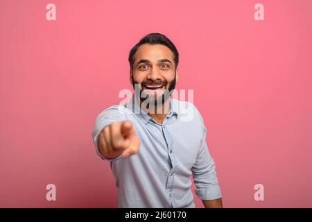 Joyful excited Indian middle-aged man in jeans shirt points fingers at the camera, surprised handsome multiracial guy choosing you, selecting viewer isolated on pink, laughs at you Stock Photo