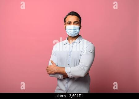 Portrait of the effective protection against coronavirus. Indian man wearing medical mask to prevent infection, respiratory illness such as flu. Indoor studio shot, pink background Stock Photo