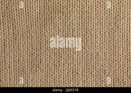 Beige knitted carpet close-up. Textile texture on a beige background. Detailed background from warm yarn. Natural wool fabric, sweater fragment. Stock Photo