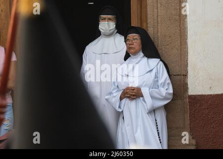 Dominican nuns watch as hooded penitents wearing traditional capirotes, hold a procession of silence on Holy Saturday, April 16, 2022 in Patzcuaro, Michoacan, Mexico. The small indigenous town retains traditions from Colonial Spanish rule including the confraternity of penitents during Holy Week. Stock Photo