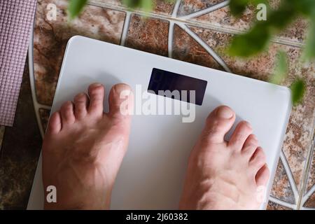 Male legs standing on white floor scales closeup Stock Photo
