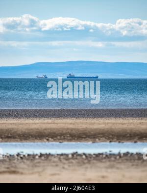 Ayr, Scotland, UK. 26th Apr, 2022. PICTURED: Oil Tankers out in the Firth of Clyde against the backdrop of the Isle of Arran. West of Scotland saw bright sunshine and blue sky at the seaside on Ayr Beach. People out walking and a horse rider takes their horse through a gallop in the cool sea water. Credit: Colin Fisher/Alamy Live News Stock Photo