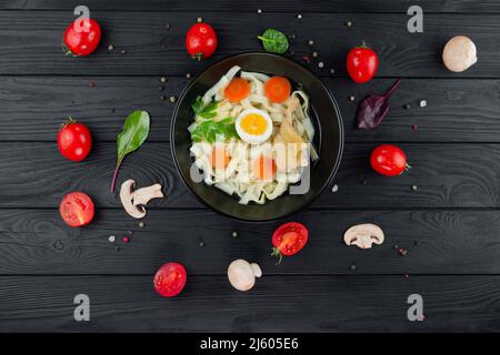 Bouillon with noodles with vegetables on a black textural background with chicken. Stock Photo