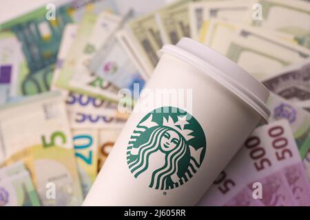 KHARKIV, UKRAINE - DECEMBER 16, 2021: White paper cup with Starbucks logo and money bills. Starbucks is the world's largest coffee house with over 20, Stock Photo