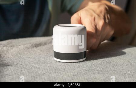 Man hand closeup removing lint from fabric with shaver. Handheld electric device for cleaning clothes from fluff, dust. High quality photo Stock Photo