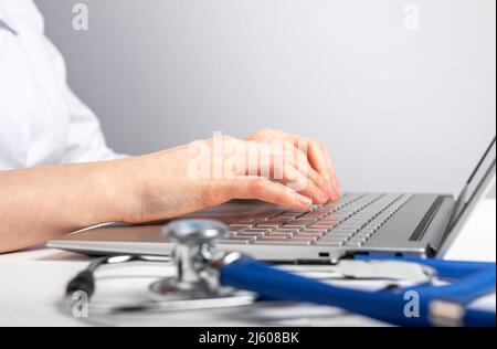 Doctor hands closeup working on laptop. Woman sitting at desk with computer and stethoscope. Patient consultation or search of medicine information. High quality photo Stock Photo