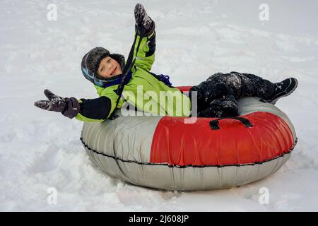 Funny Caucasian boy 5 years old rides in winter on a big inflatable cheesecake Stock Photo