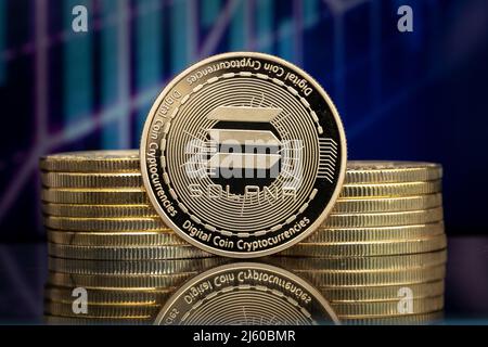 Solana SOL cryptocurrency physical coin and blurry price charts. Stock Photo
