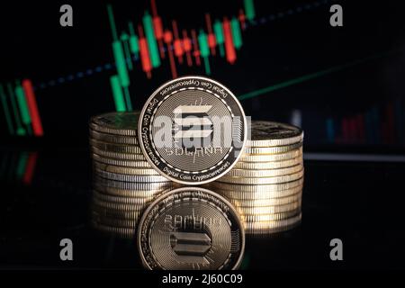 Solana SOL cryptocurrency physical coin and blurry price charts. Stock Photo