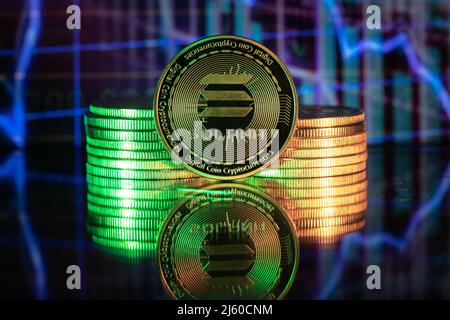 Solana SOL cryptocurrency physical coin and blurry price charts. Stock Photo