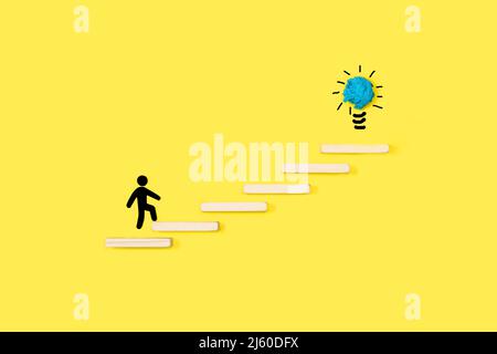 Man sign climbing wooden steps with a light bulb at the top on a yellow background with copy space Stock Photo