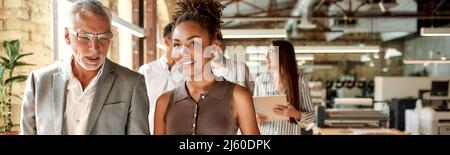 Sharing ideas. Two business experts discussing something while walking with colleagues through the office corrido Stock Photo