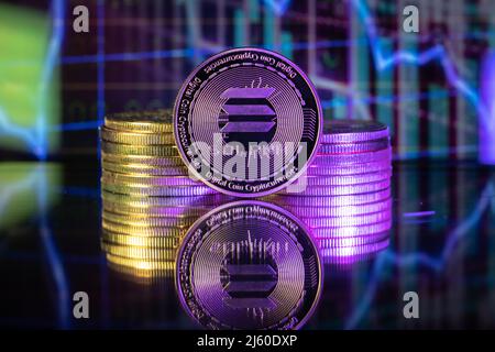 Solana SOL cryptocurrency physical coin and blurry price charts. Stock Photo