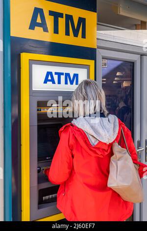 Woman using an ATM/cash machine in Dingle, County Kerry, Ireland. Stock Photo