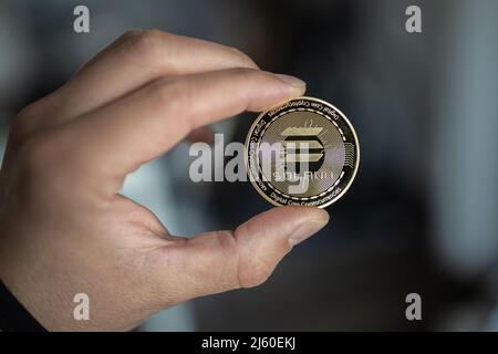 Solana SOL cryptocurrency physical coin held between two fingers. Stock Photo